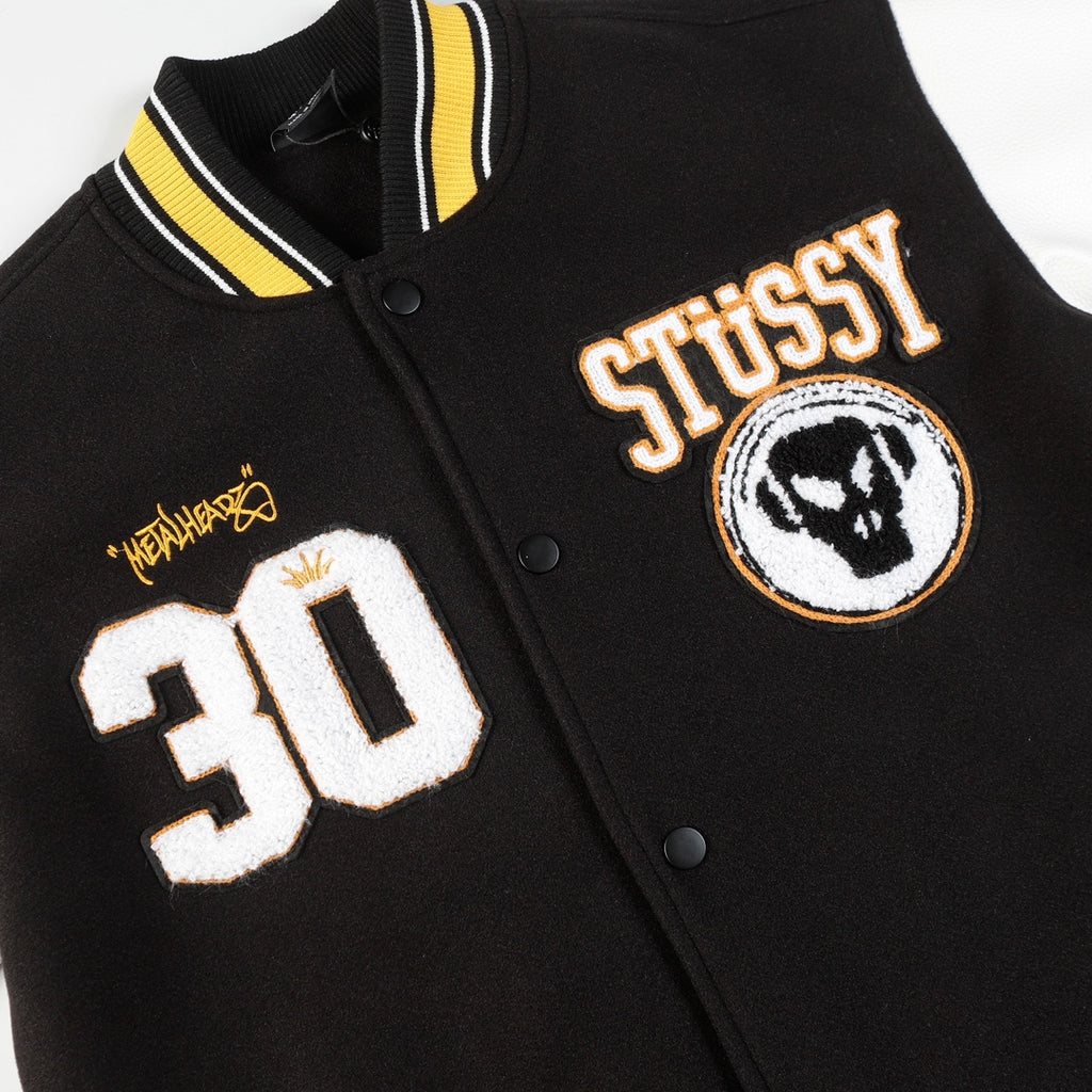 Black varsity jacket close-up with Stüssy crest patch and 30 number graphic