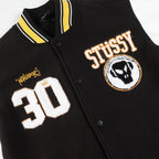 Black varsity jacket close-up with Stüssy crest patch and 30 number graphic