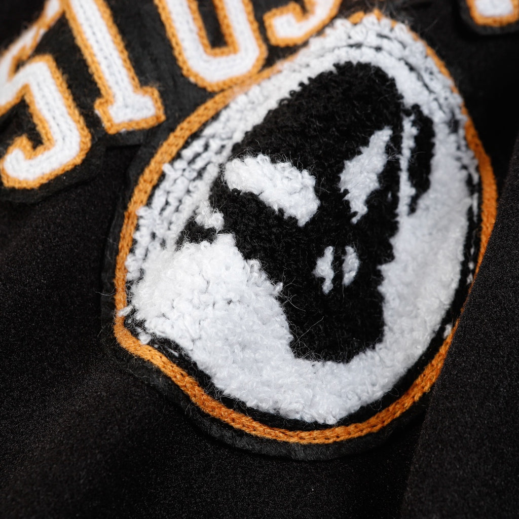 Black varsity jacket close-up of crest patch with orange outline and white fill