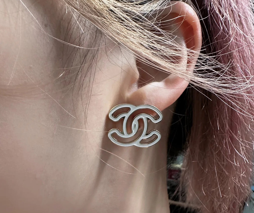 CC logo stud earrings on ear, silver-toned outline with black enamel