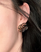 CC logo stud earrings on ear, black enamel with gold-toned outline