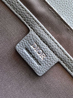 Dior bag strap attachment with embossed logo on gray textured leather.