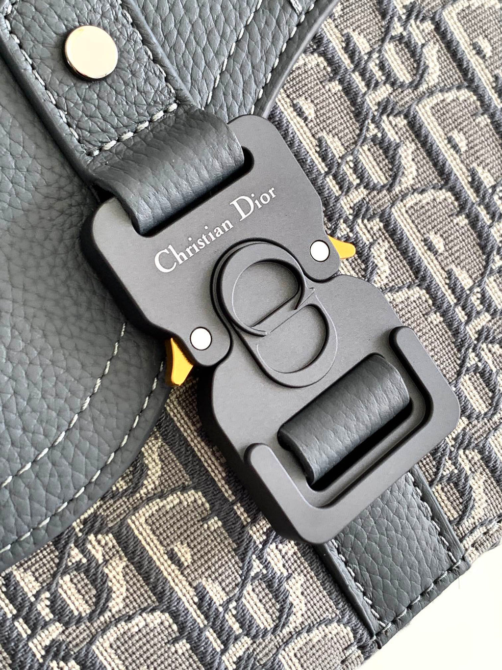 Dior bag key fob charm on textured gray leather with metal clasp and engraving.