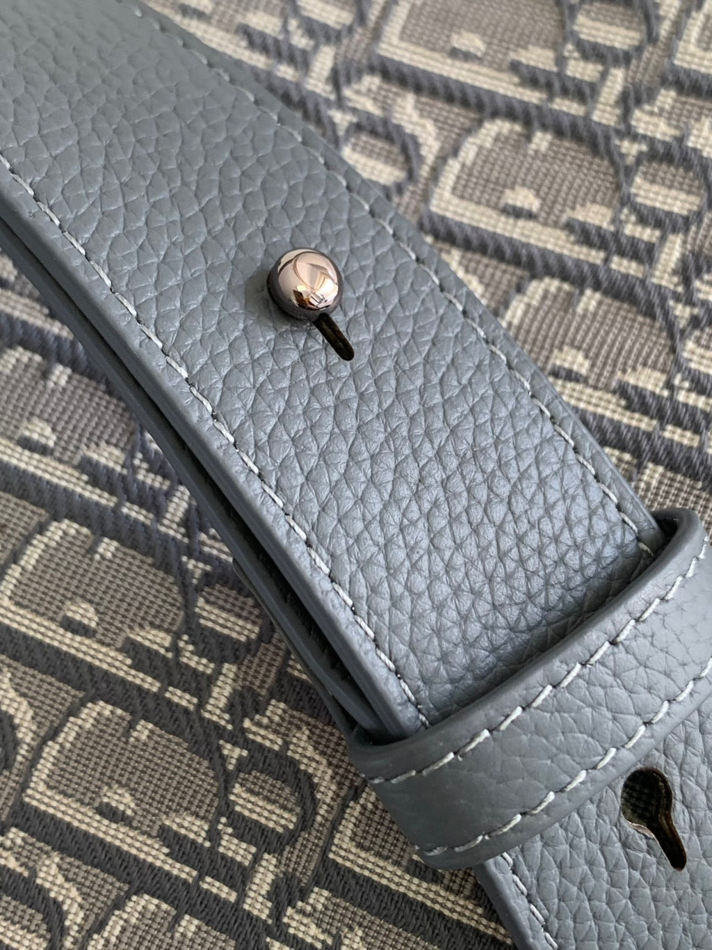 Dior crossbody bag strap end with snap button on gray textured leather trim.