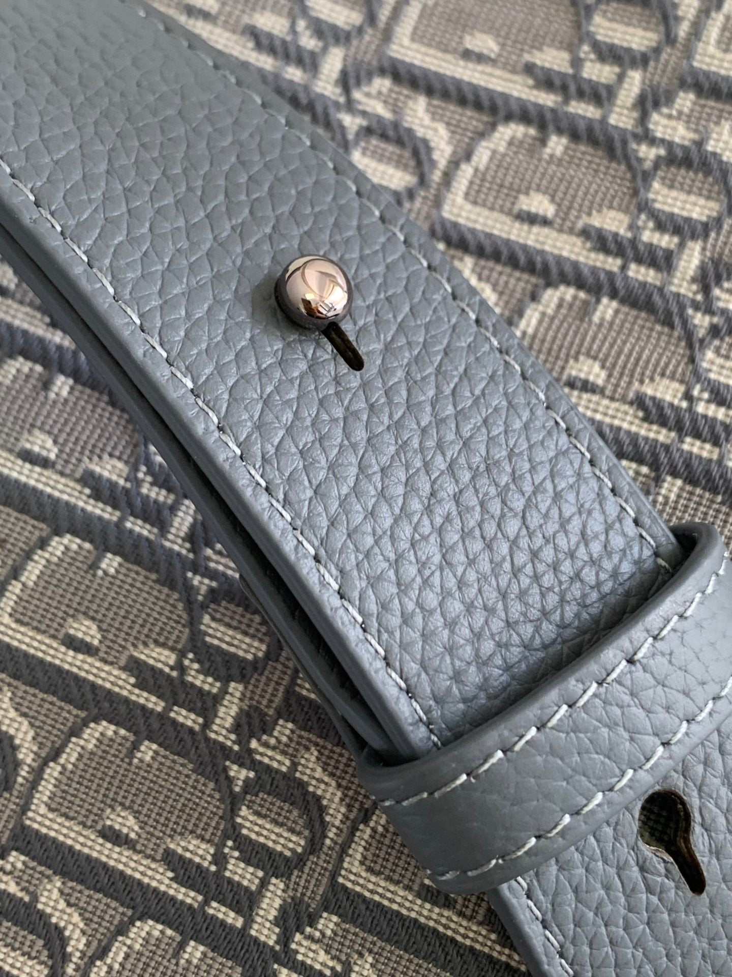 Dior crossbody bag strap end with snap button on gray textured leather trim.