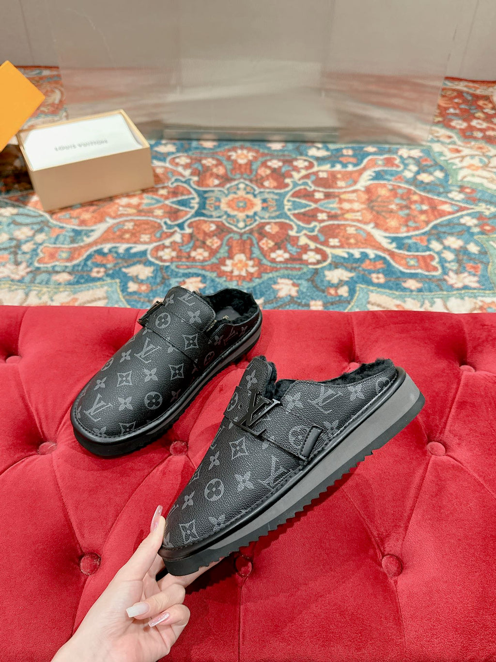 Black Louis Vuitton monogram slide sandals held on red cushion, pair view
