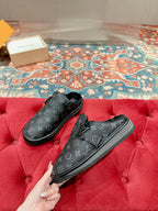 Black Louis Vuitton monogram slide sandals held on red cushion, pair view