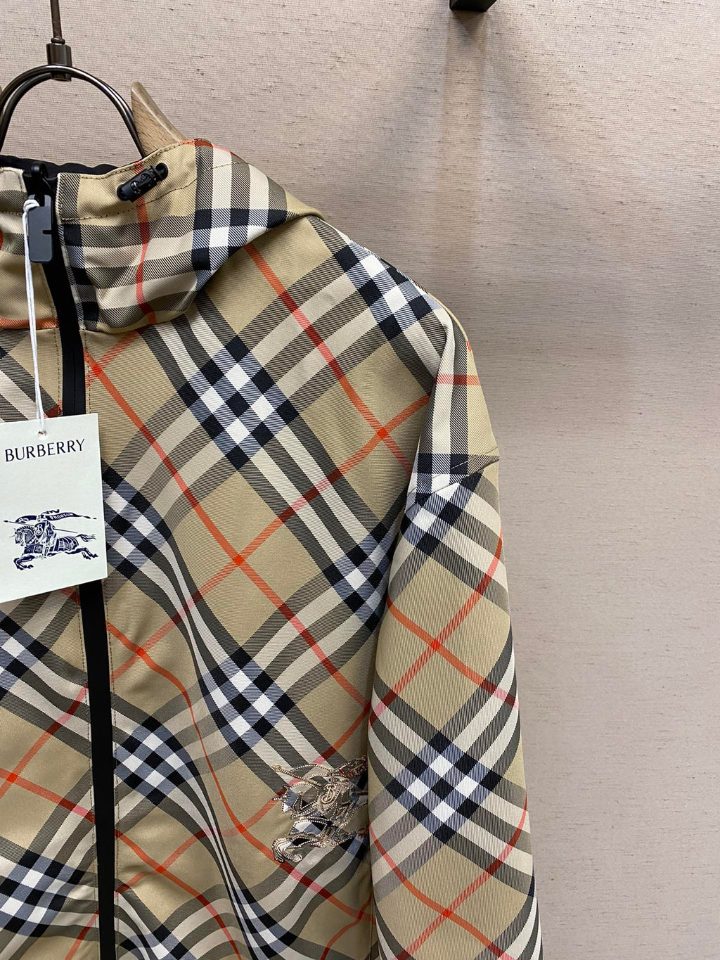 Plaid hooded jacket sleeve with embroidered emblem on beige, navy, and red fabric