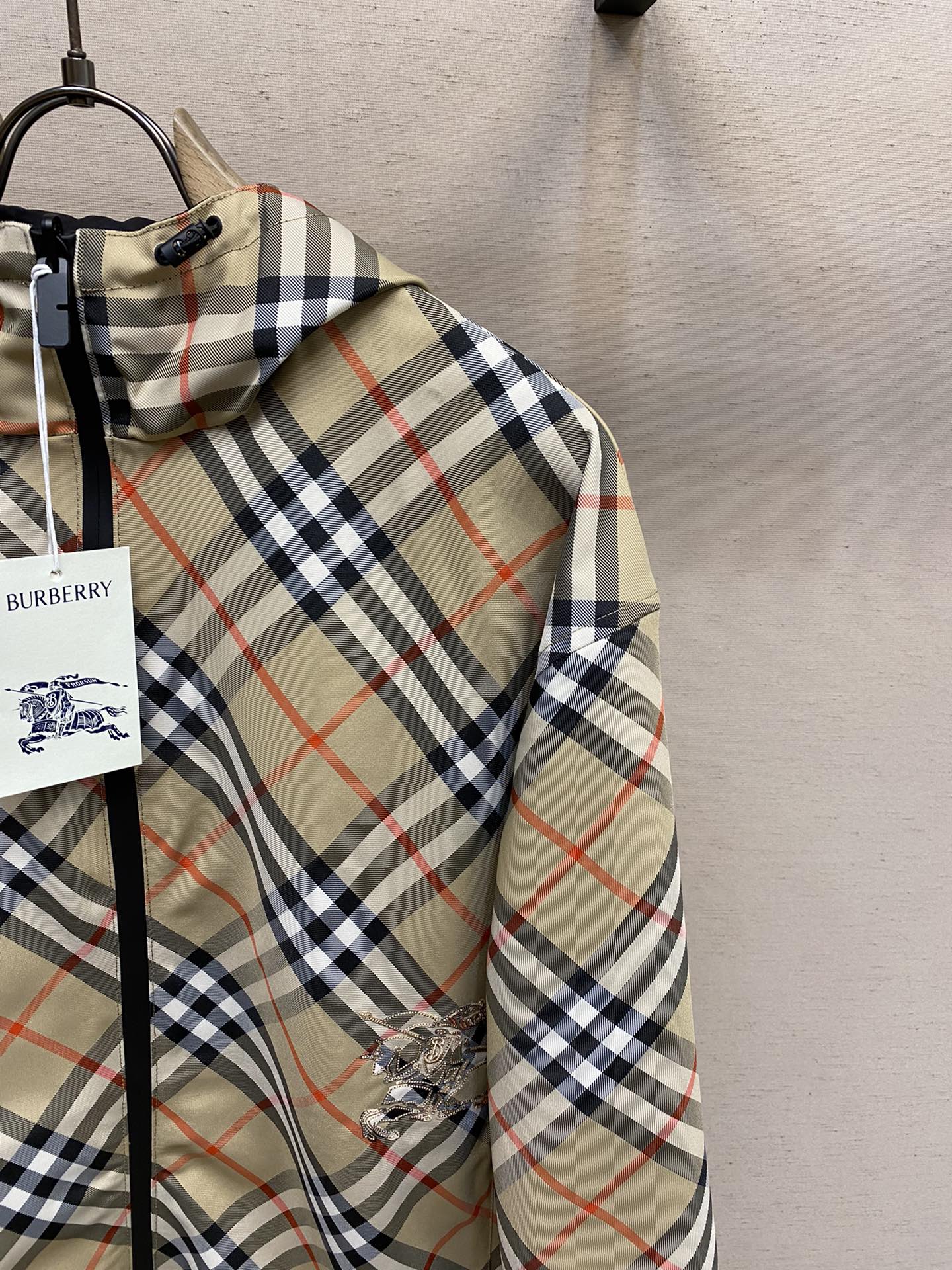 Plaid hooded jacket sleeve with embroidered emblem on beige, navy, and red fabric