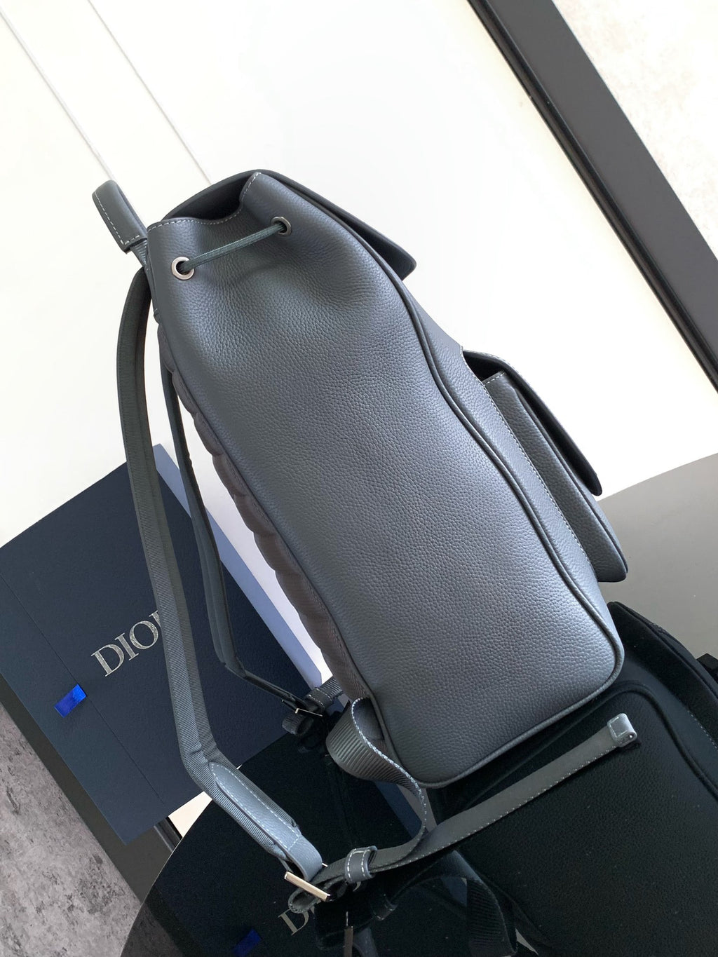 Men's gray leather backpack, side view with adjustable straps and top handle