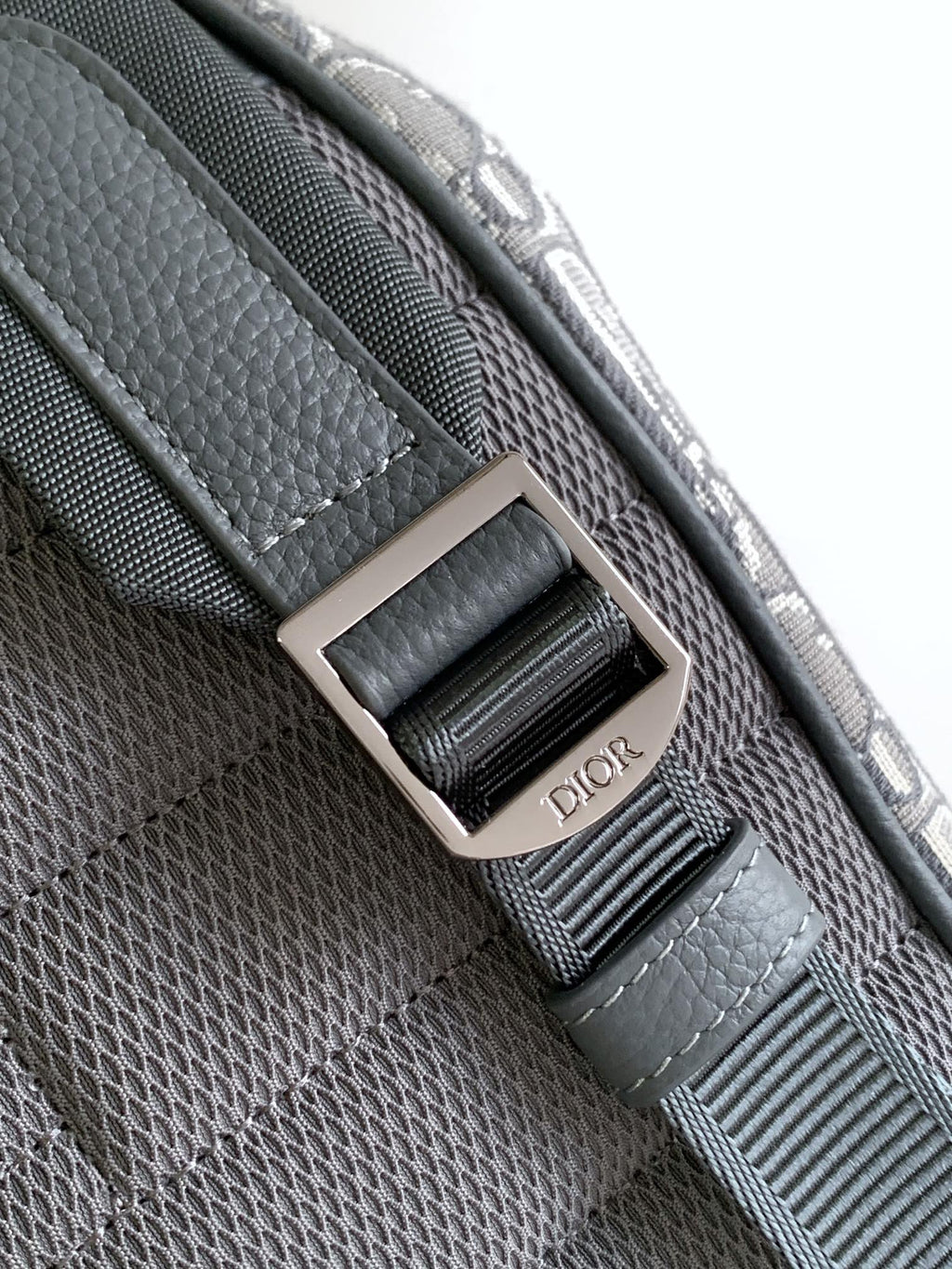 Dior bag close-up of gray woven strap with silver square buckle and Dior lettering