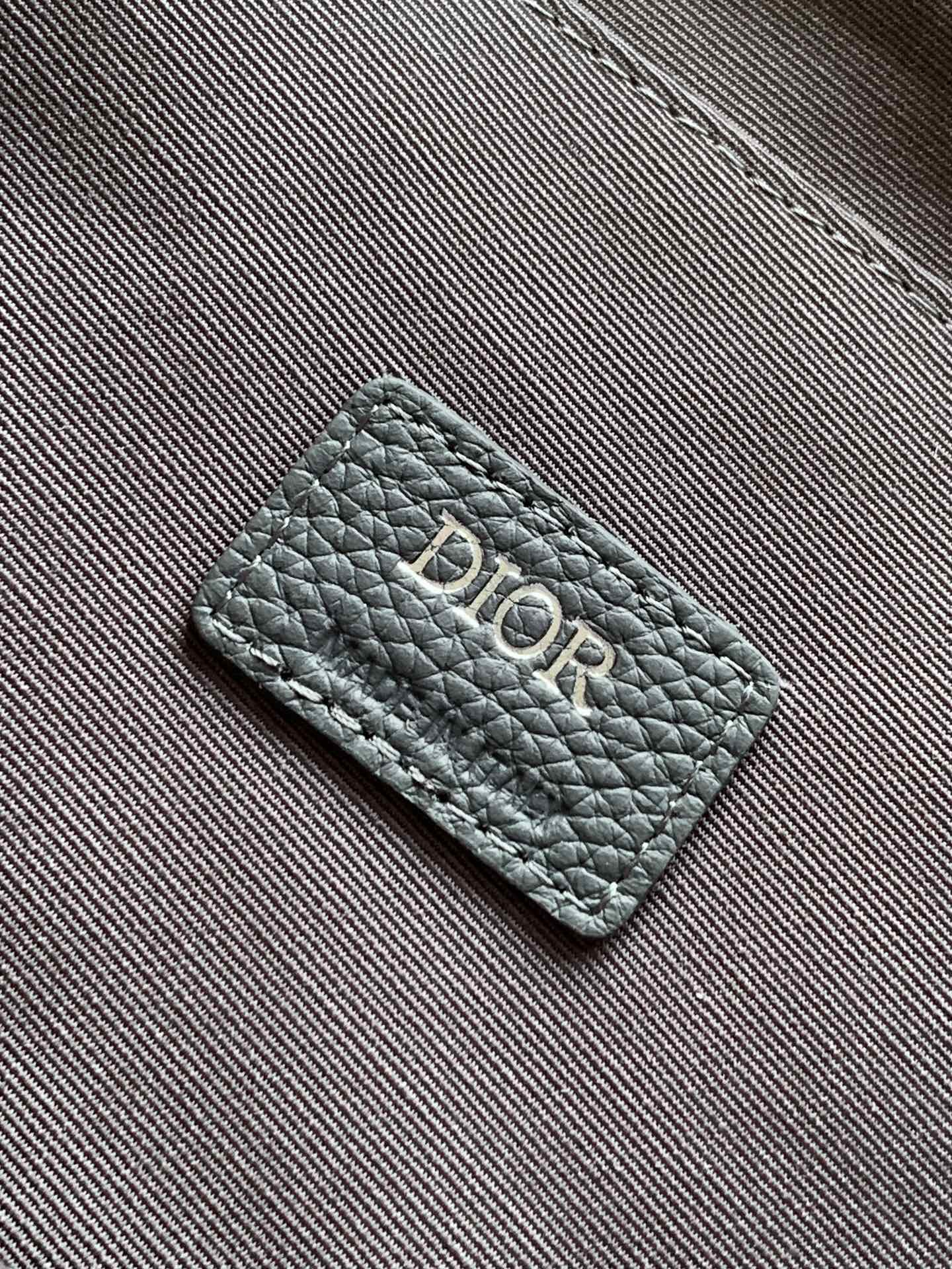 Embossed gray Dior logo patch on textured leather bag strap