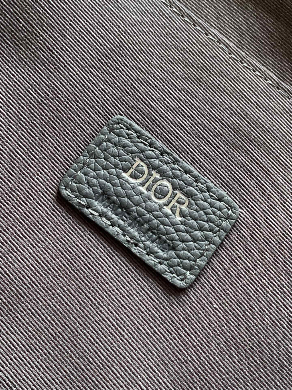 Dior bag leather tag with Dior logo on gray textured exterior