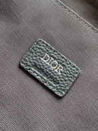 Dior bag leather tag with Dior logo on gray textured exterior