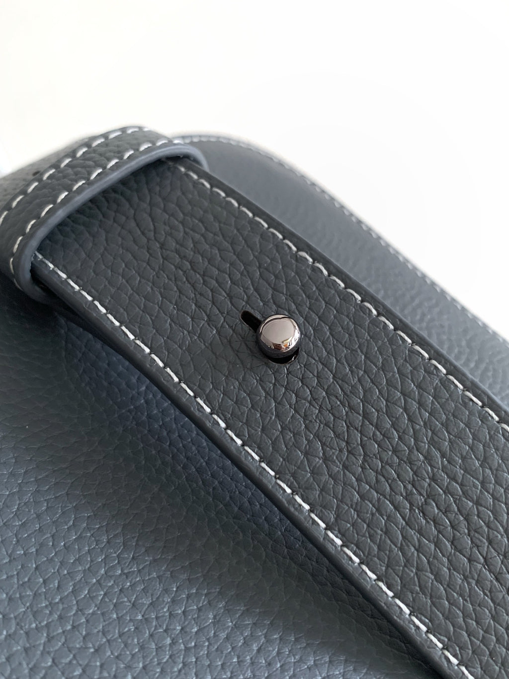 Blue-gray leather bag edge with contrast stitching and snap button detail