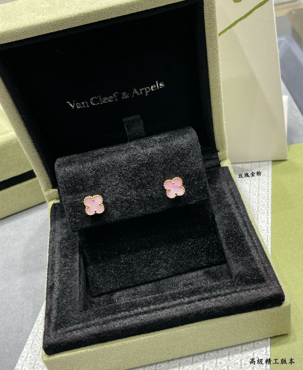 Four-leaf clover stud earrings with pink enamel resting on black velvet