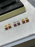 Clover stud earrings with gold, silver, and red enamel motifs laid on jewelry tray