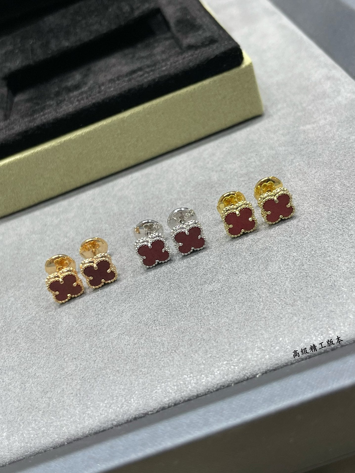 Clover stud earrings with gold, silver, and red enamel motifs laid on jewelry tray