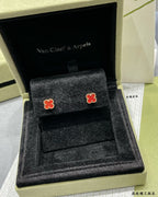 Pair of red enamel clover stud earrings displayed on a black jewelry tray