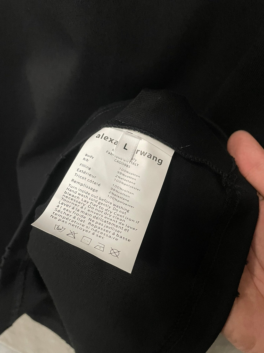 Black T-shirt care label on inside neck seam, held in hand