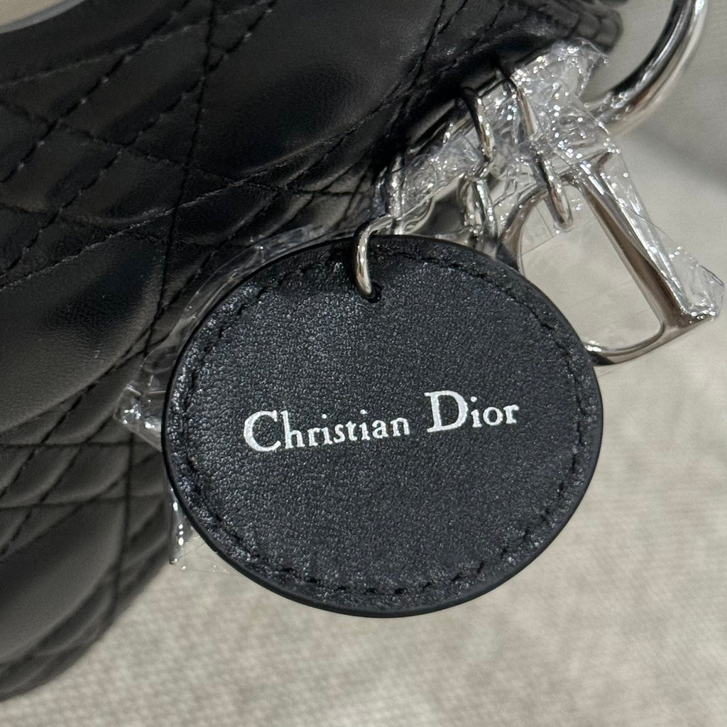 Black leather Dior handbag round logo tag reading Christian Dior, with silver ring.