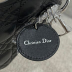 Black leather Dior handbag round logo tag reading Christian Dior, with silver ring.
