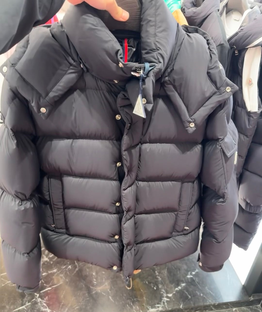 Long puffer jacket in dark color with hood, front button placket and quilted blocks