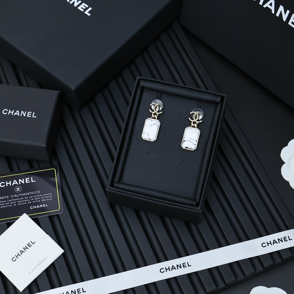 Gold-tone drop earrings with white marbled pendants in a black presentation box