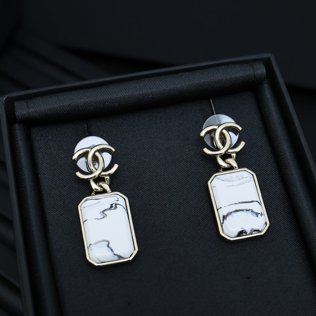 Gold-tone drop earrings with white marbled rectangular pendants in a black box
