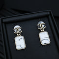 Gold-tone drop earrings with white marbled rectangular pendants in a black box