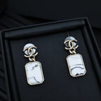 Gold-tone drop earrings with white marbled rectangular pendants in a black box