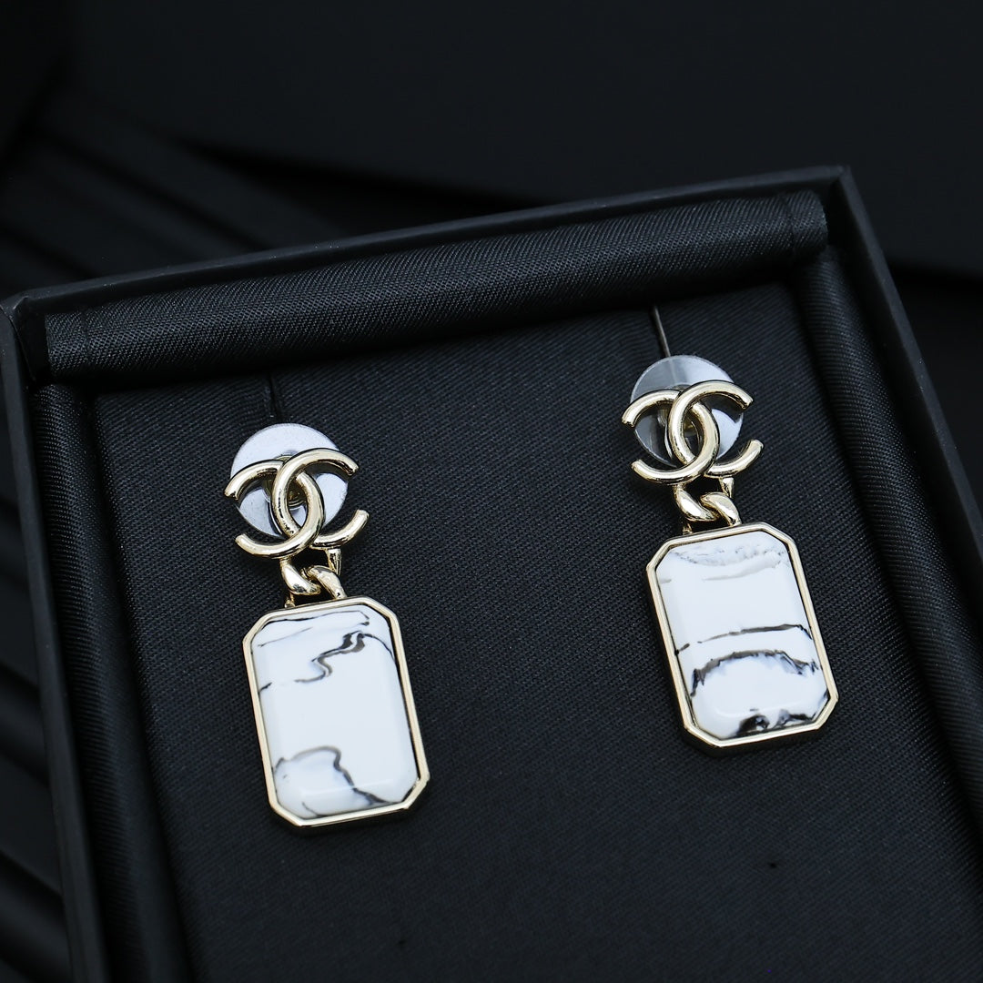 Gold-tone drop earrings with white marbled rectangular pendants in a black box