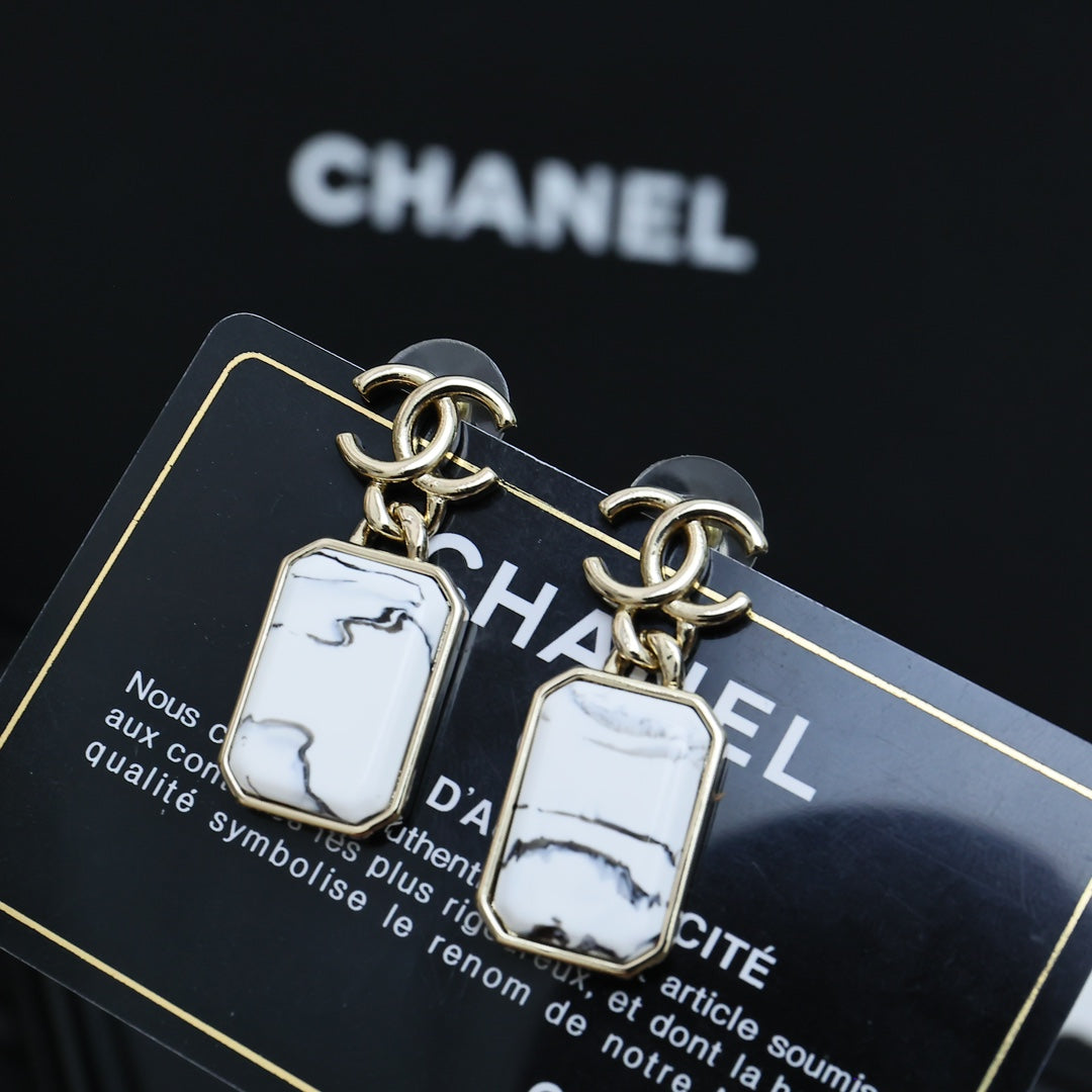Gold-tone drop earrings with white marbled rectangular pendants on a card