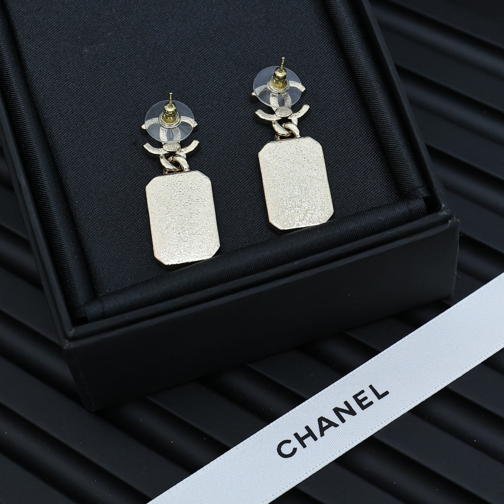 Gold-tone drop earrings with white marbled square pendants on a black display