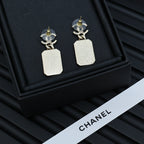 Gold-tone drop earrings with white marbled square pendants on a black display