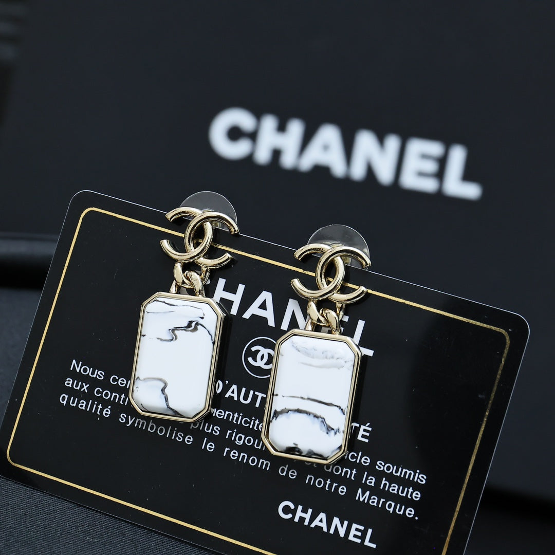 Gold-tone drop earrings with white marbled rectangular pendants on a card