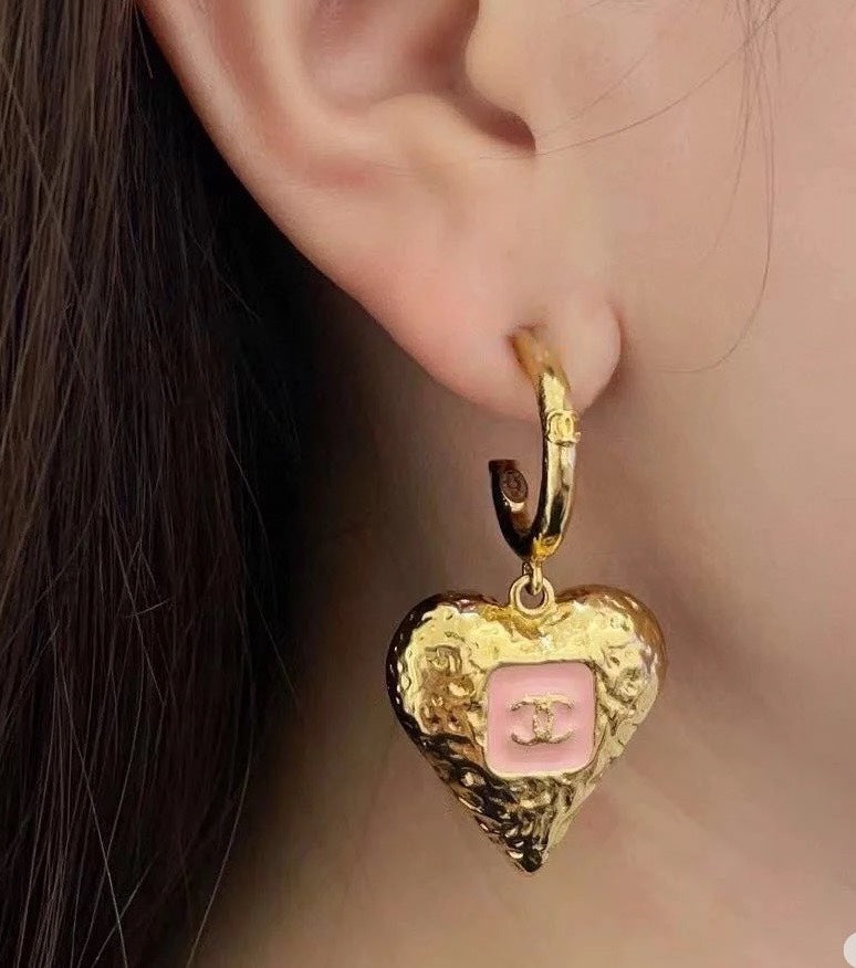 Gold-tone heart drop earring with pink enamel logo on a hoop earlobe.