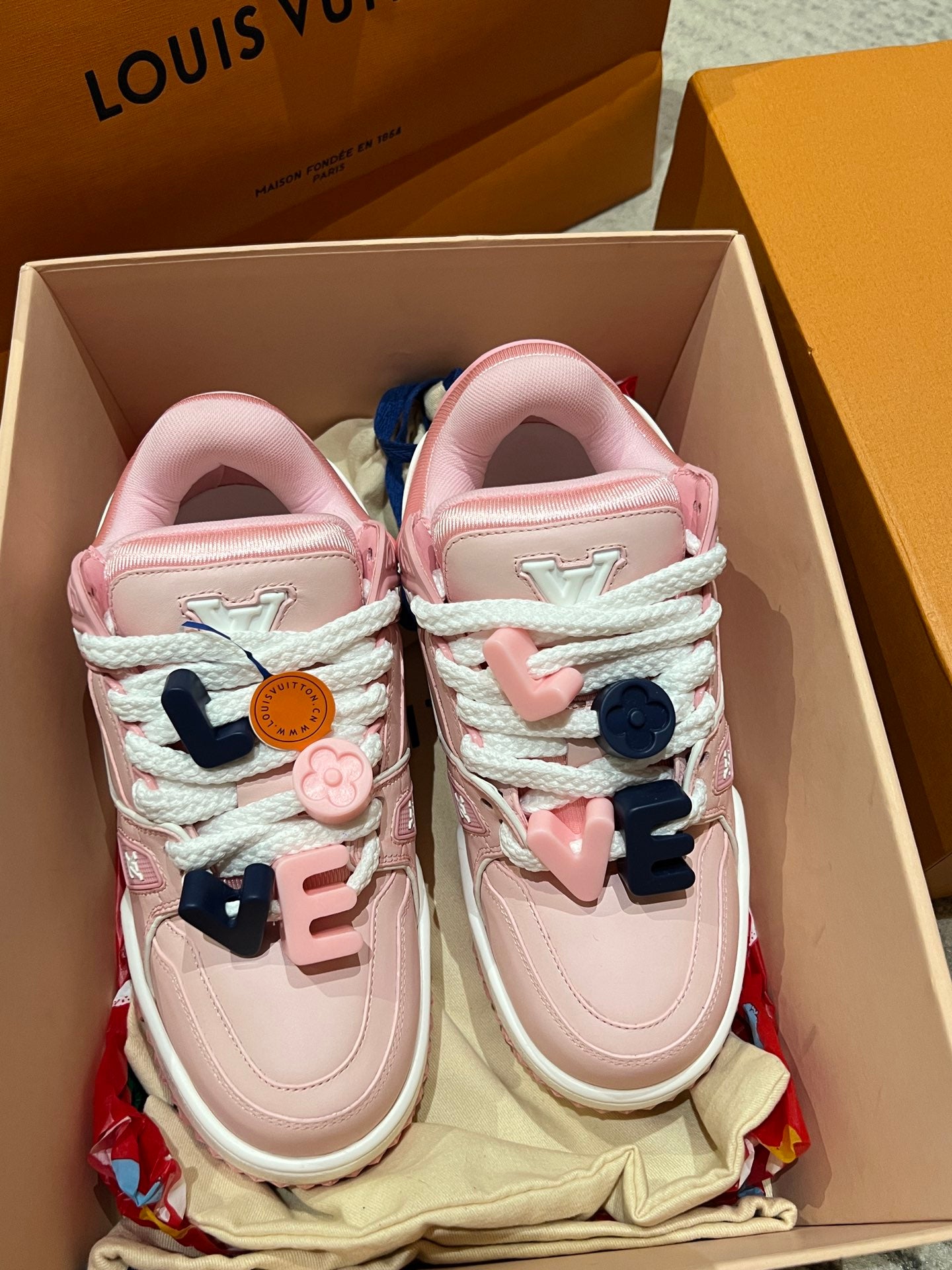 Pink low-top sneakers with white laces, blue and pink strap charms, shoebox view