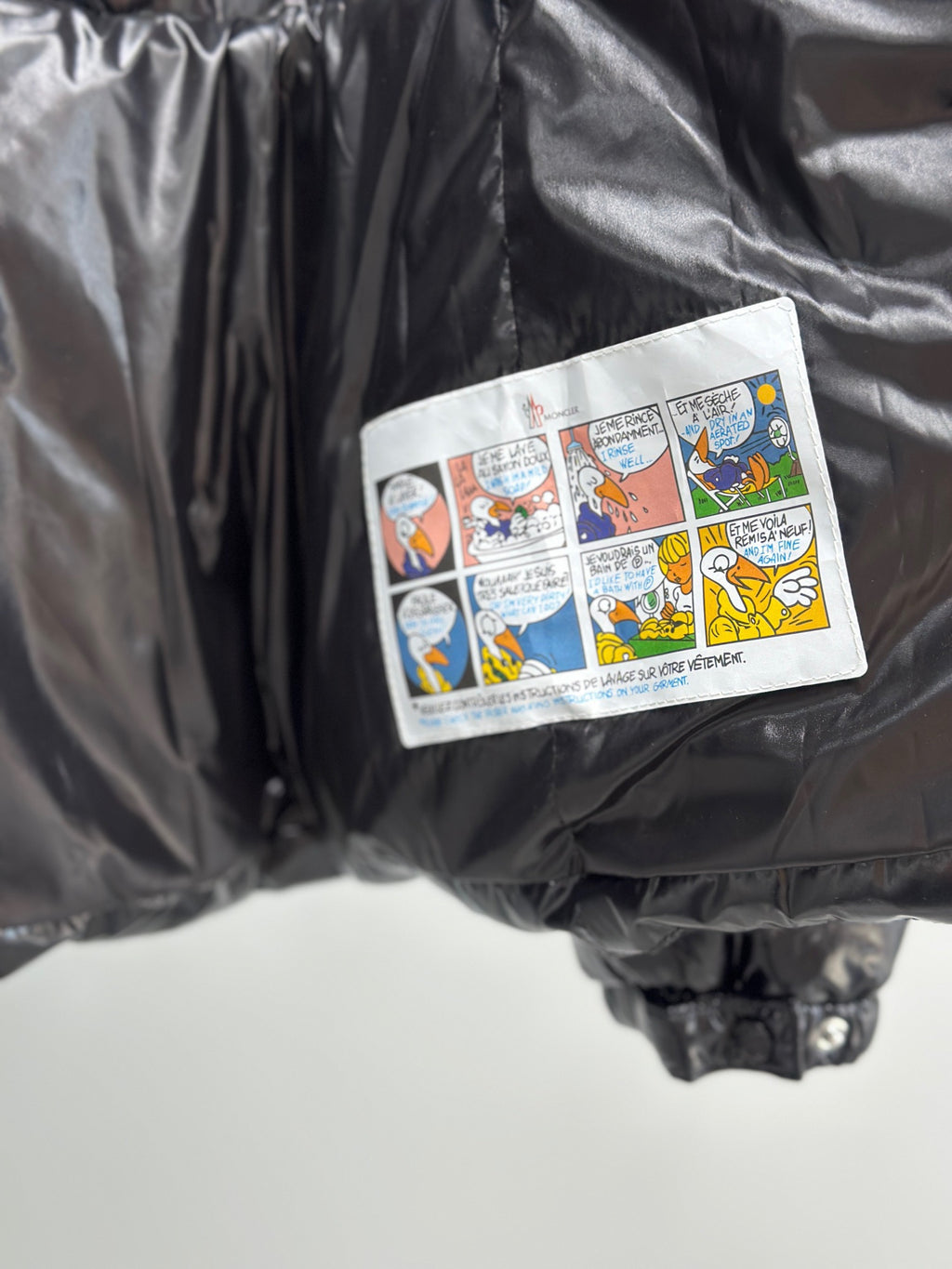 Cartoon-style patch label on pocket of glossy black puffer jacket