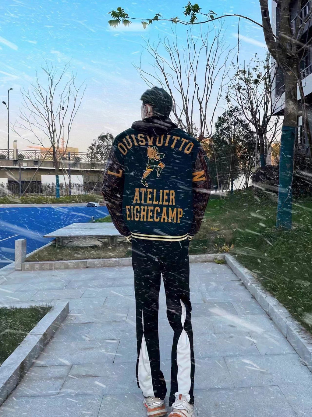 Back of green varsity jacket with large brown text graphic, striped waistband, patterned sleeves