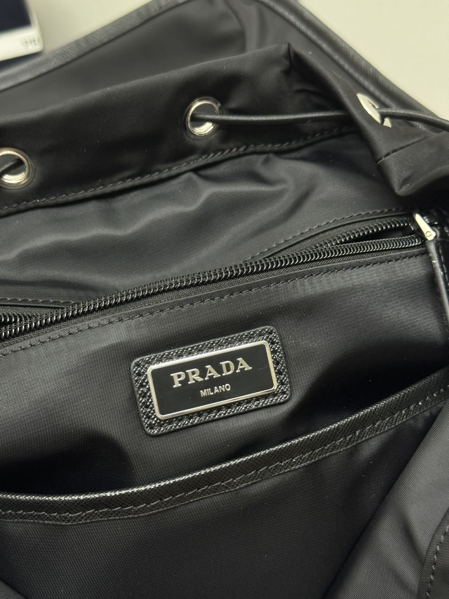 Prada Milano logo patch on black backpack front pocket with zipper