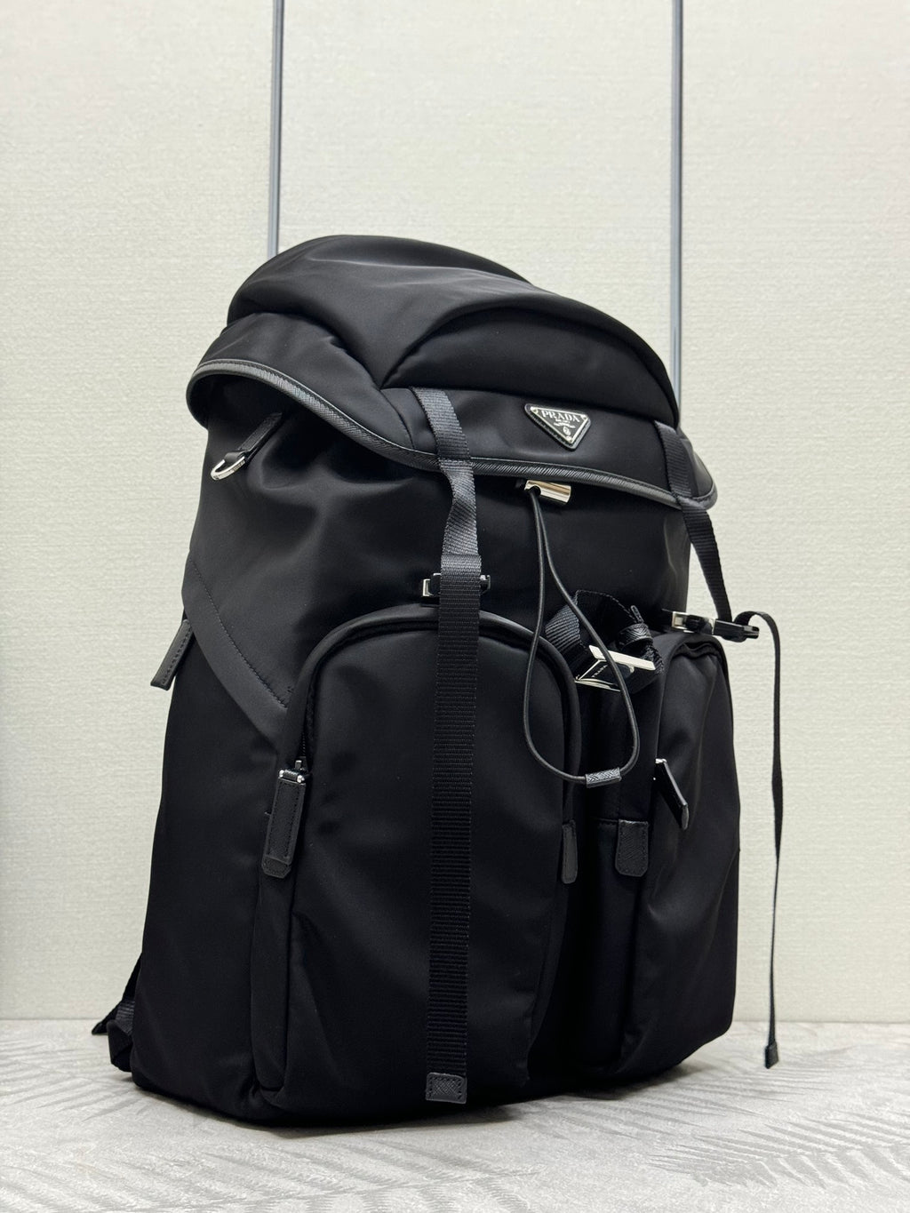 Prada black backpack with top flap, side pockets, and hanging strap details