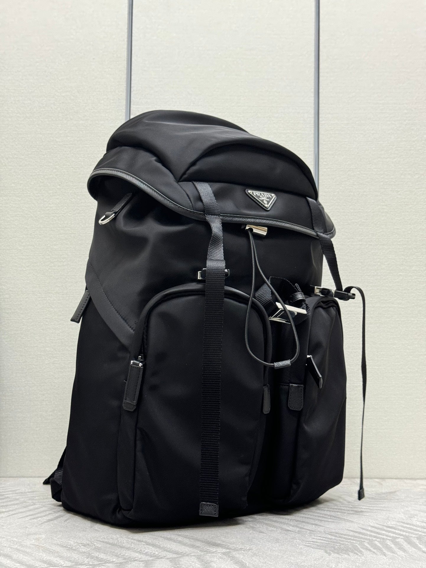 Prada black backpack with top flap, side pockets, and hanging strap details