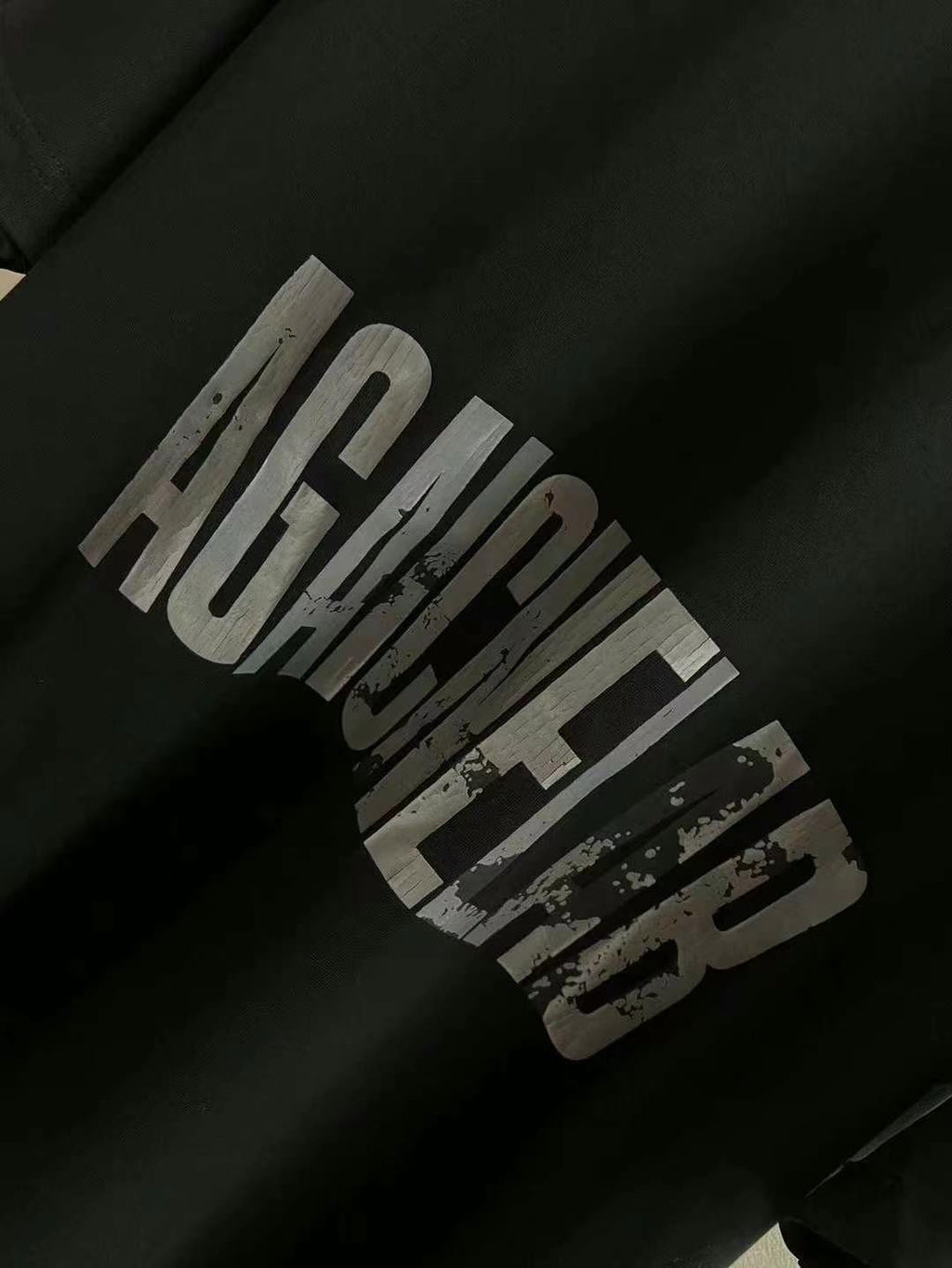 Close-up of black T-shirt sleeve with distressed “AGAINST” graphic print