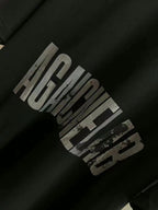 Close-up of black T-shirt sleeve with distressed “AGAINST” graphic print