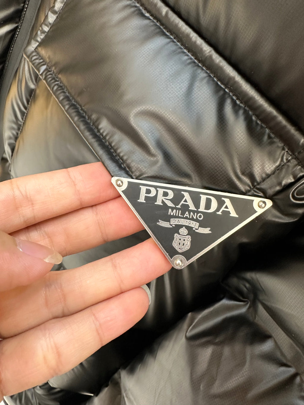 Prada label on dark puffer jacket fabric with metal logo tag