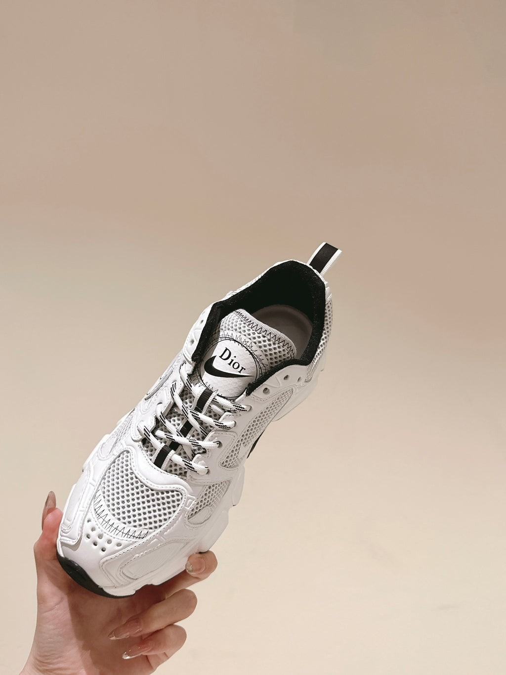 White sneaker held in hand with Dior logo tongue and black heel trim
