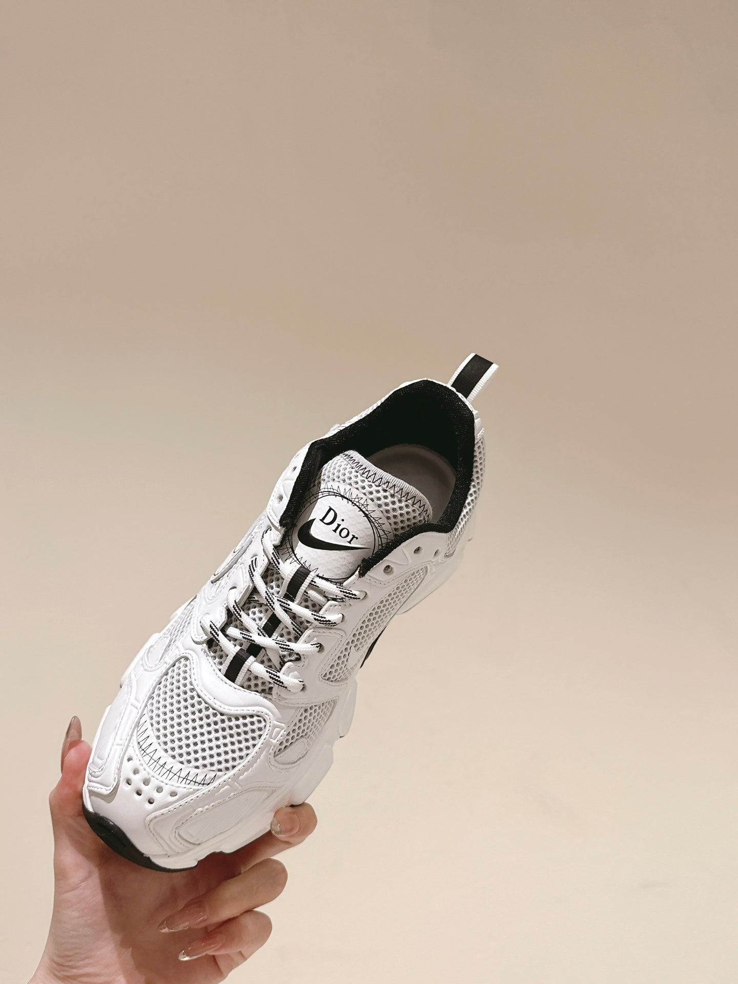 White sneaker held in hand with Dior logo tongue and black heel trim