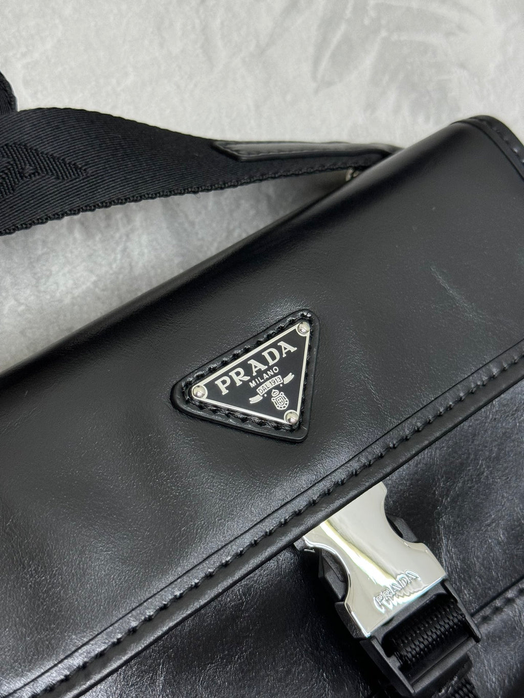 Prada bag close-up: black flap with silver logo plaque and stitched edge
