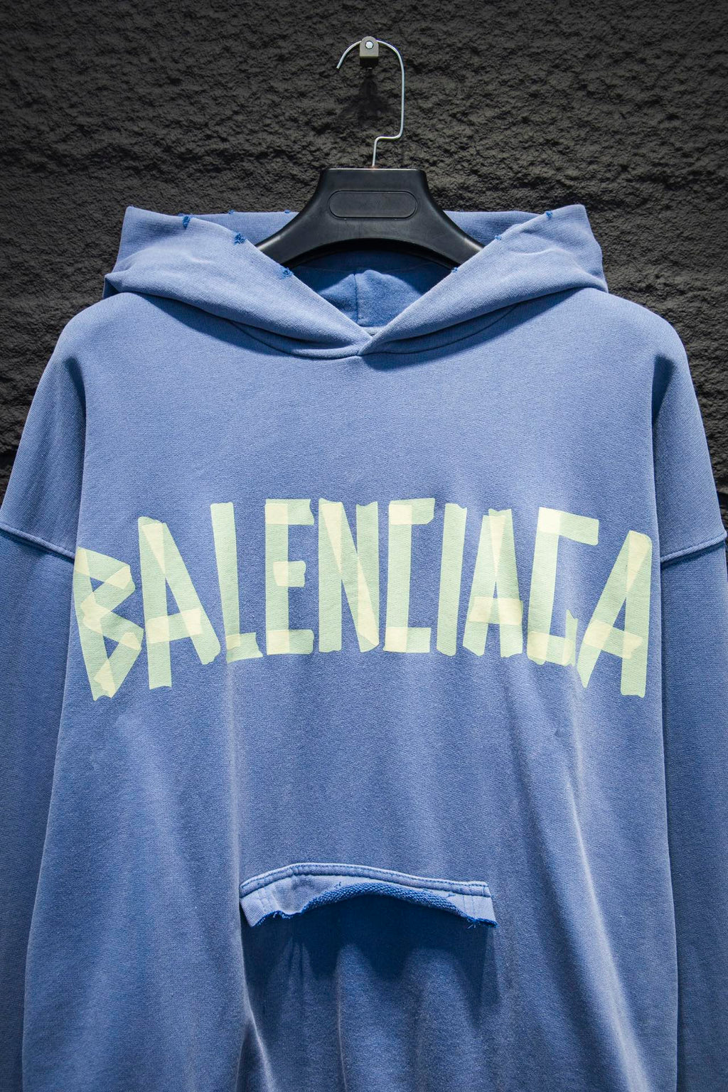 Light blue hoodie with hood and large front graphic text; front pocket opening detail visible